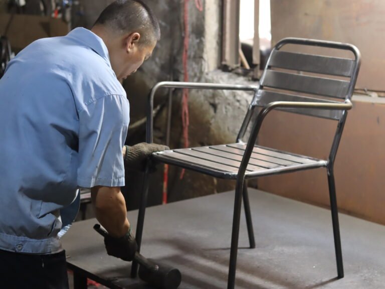 Fabrieksarbeider die een afgewerkt metalen frame van een buitenstoel controleert
